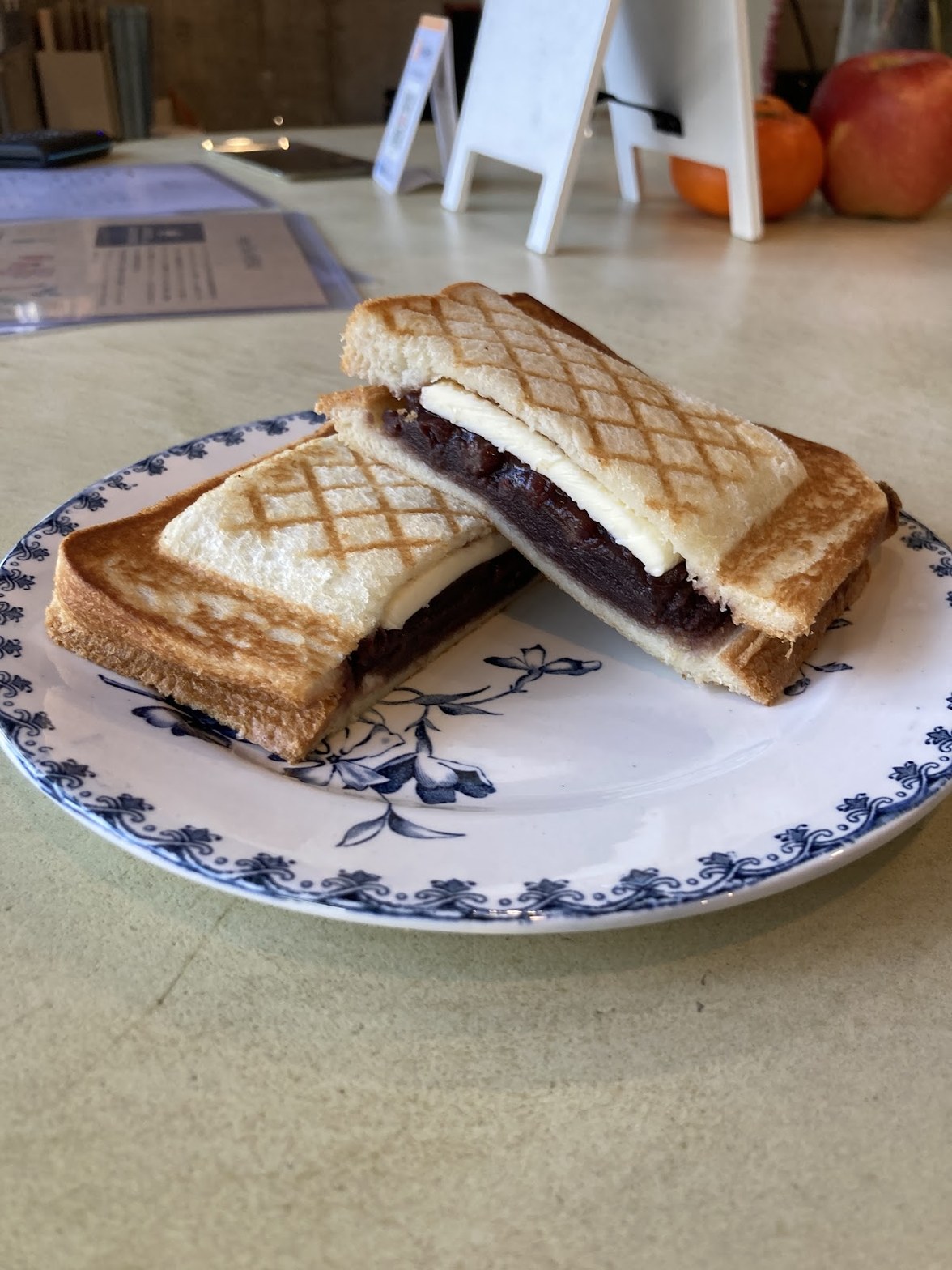 格子模様に焼かれたホットサンドがふたつ重なり、赤絵の伊万里風の皿に盛られてテーブルに置かれている。断面からとろけたチーズが見える。