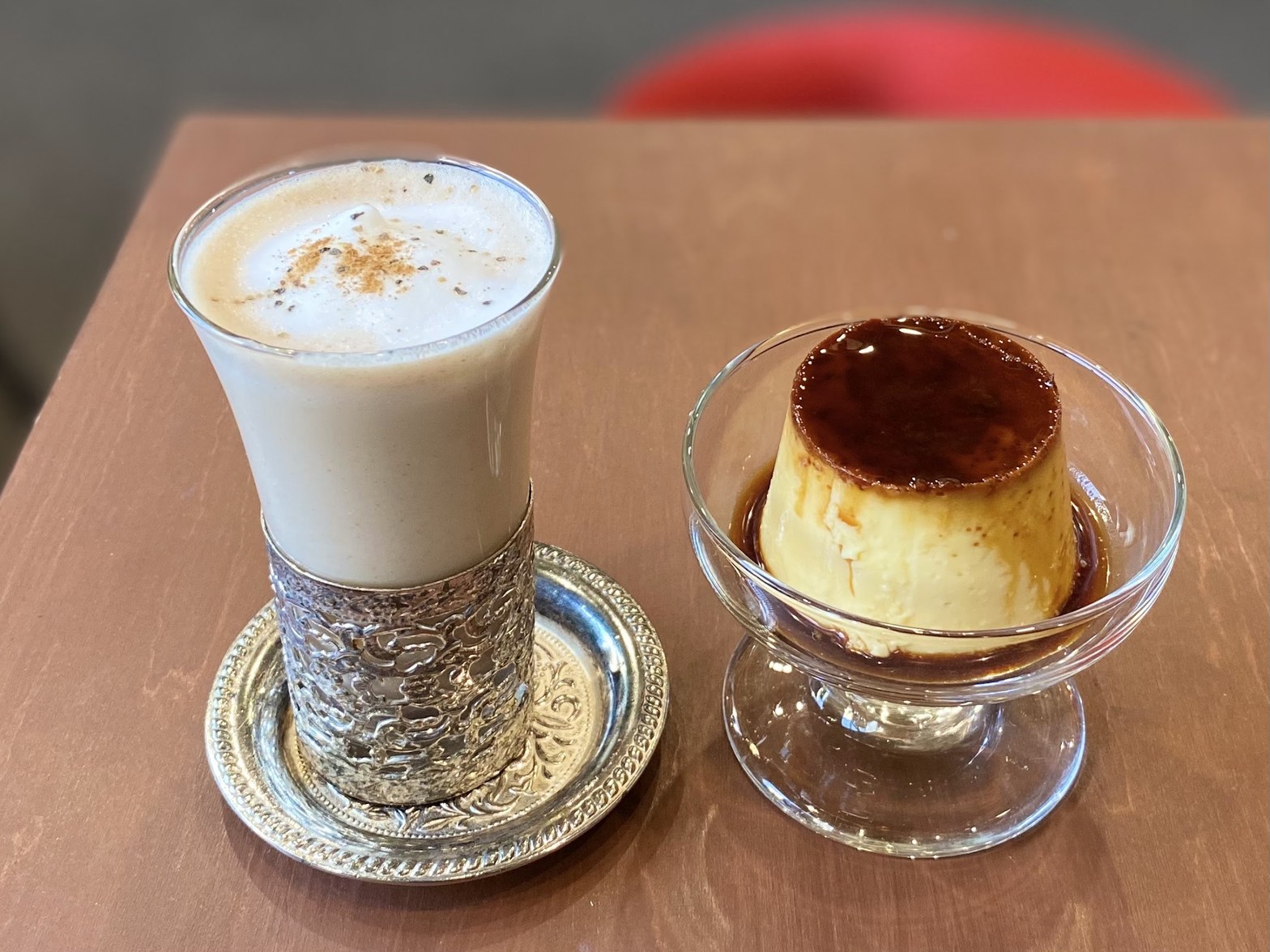 銀細工のホルダーに入ったミルキーなチャイと、ガラスの器に盛られた焼きプリン。カラメルソースが表面に広がり、テーブルに並んで置かれている。